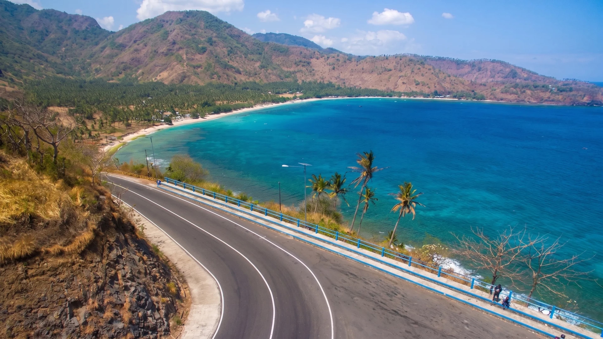 A coastal road curving along a hillside overlooking the sea in Lombok